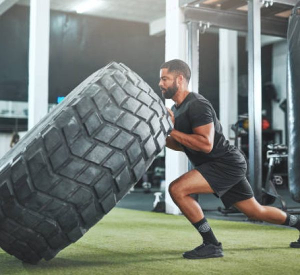 Shot of a young man flipping a heavy tyre in a gym